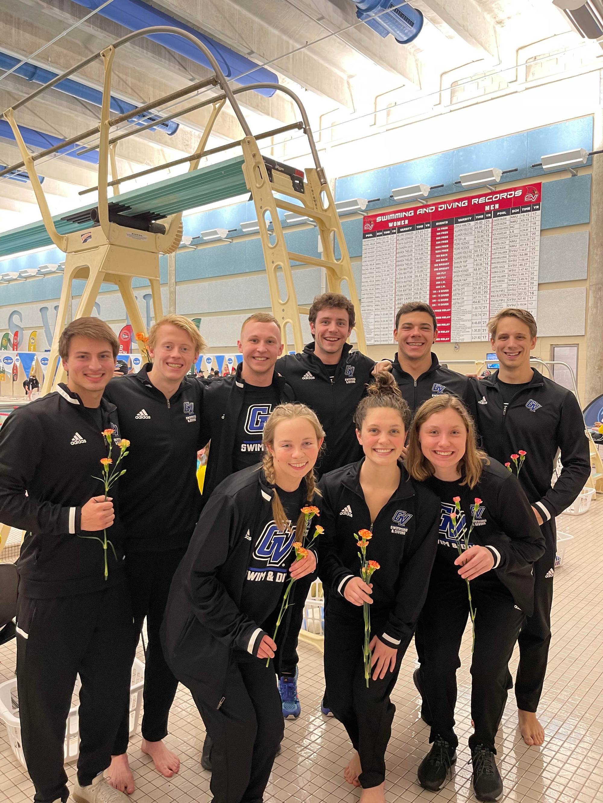 male and female identifying student athletes pose for a picture holding flowers on senior night, picture taken on pool deck